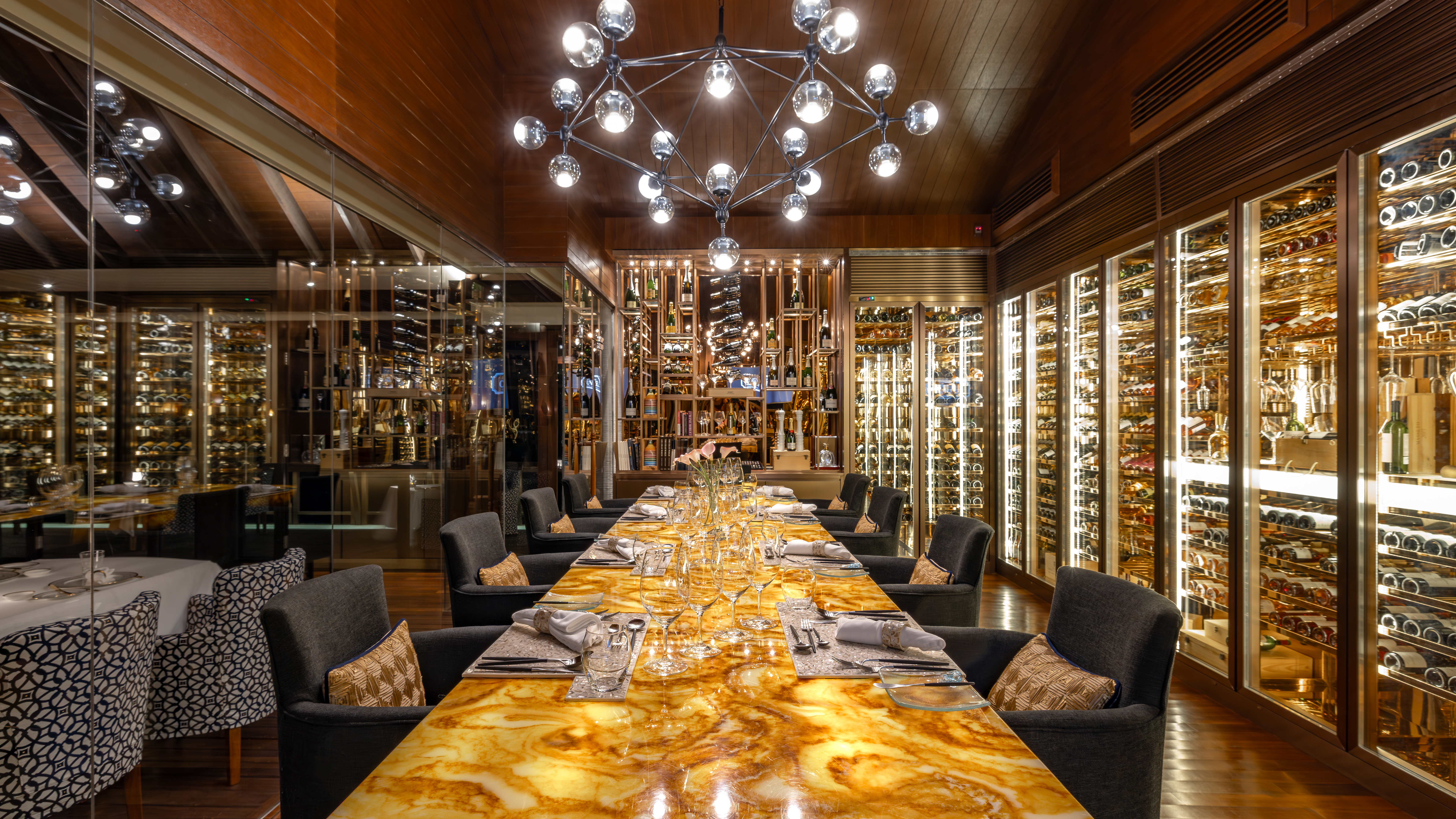 Long marble dining table with chairs, surrounded by cabinets full of wine bottles