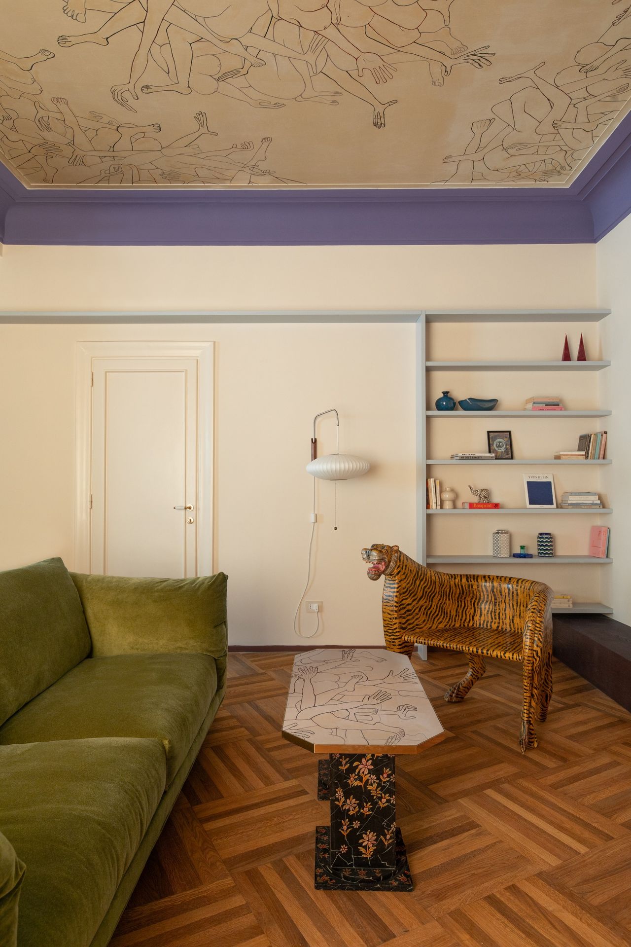 A living room with green sofa, parquet flooring, a tiger-style chair and mural painted on the ceiling