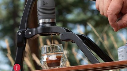 A black tripod style portable espresso maker being used to make a shot of espresso with crema outside