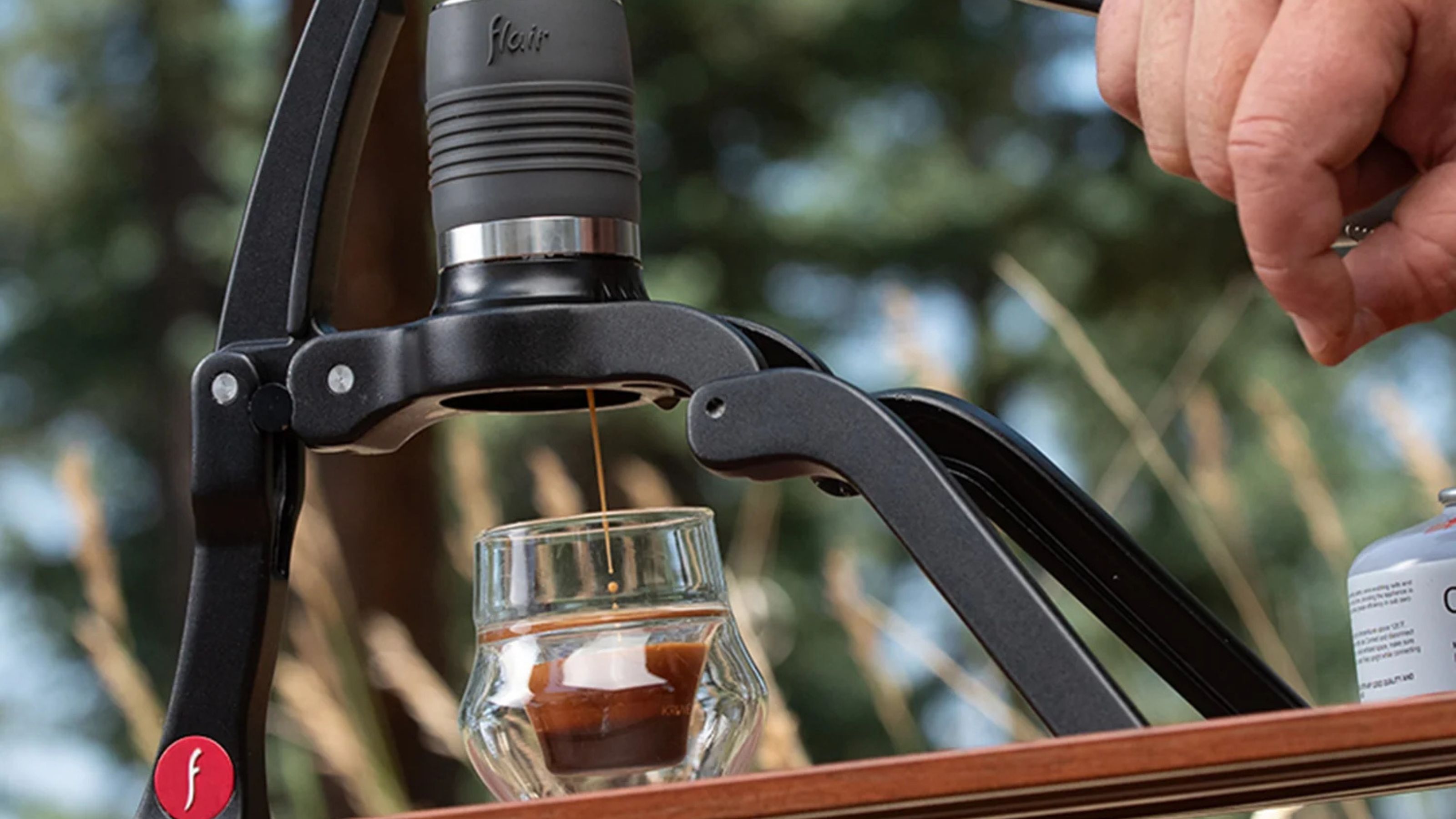 A black tripod style portable espresso maker being used to make a shot of espresso with crema outside