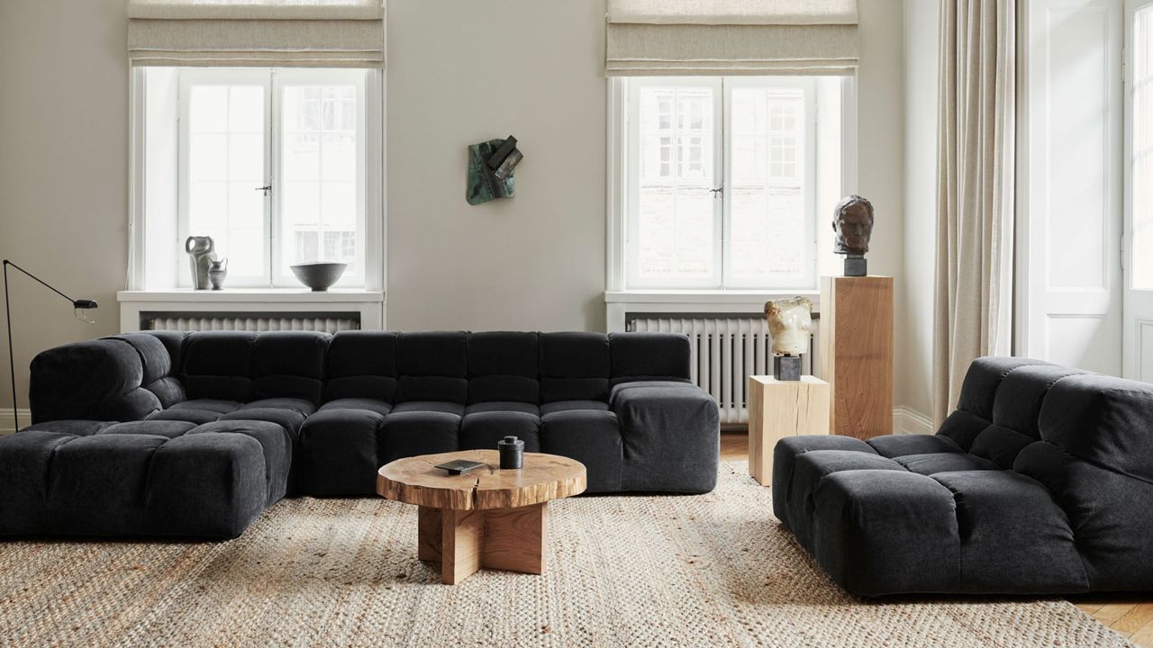 modern living room with dark gray sofas, light gray walls, jute rug, round timber coffee table, and wooden plinths