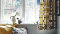 Window sill with mustard yellow and gray patterned curtains and mustard yellow and grey cushions