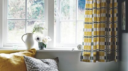 Window sill with mustard yellow and gray patterned curtains and mustard yellow and grey cushions