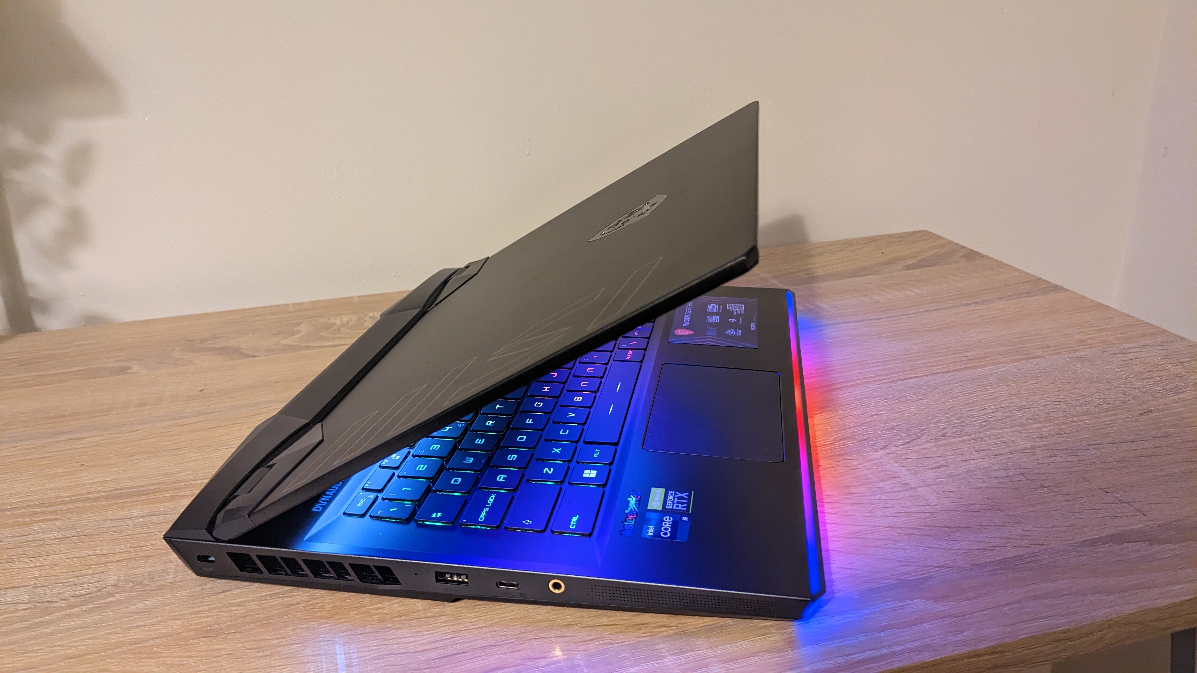 The MSI Raider GE67 HX photographed on a wooden desk with RGB lighting turned on.