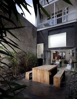 Courtyard with wooden park table and bench on grey concrete floor, surrounded by decorative blue/grey slates. Grey french doors leading to the interior