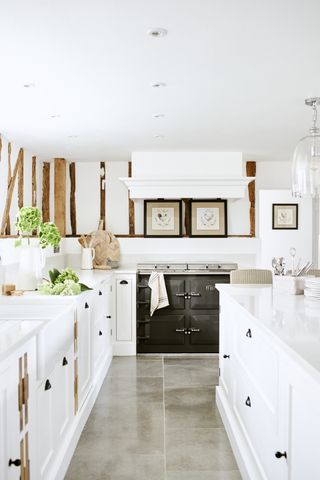 White kitchen cabinet colors with black handles and Aga, gray stone flooring and a timbered white wall.