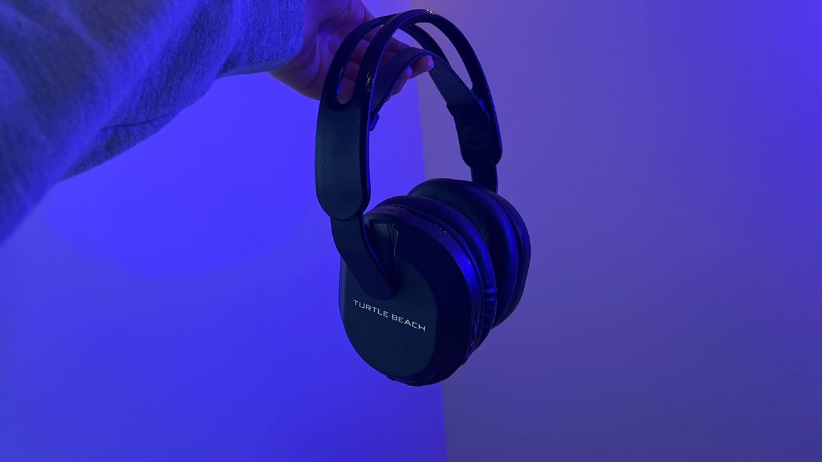 Turtle Beach Stealth 500 gaming headset being held by a reviewer against a wall with blue lighting