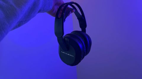 Turtle Beach Stealth 500 gaming headset being held by a reviewer against a wall with blue lighting