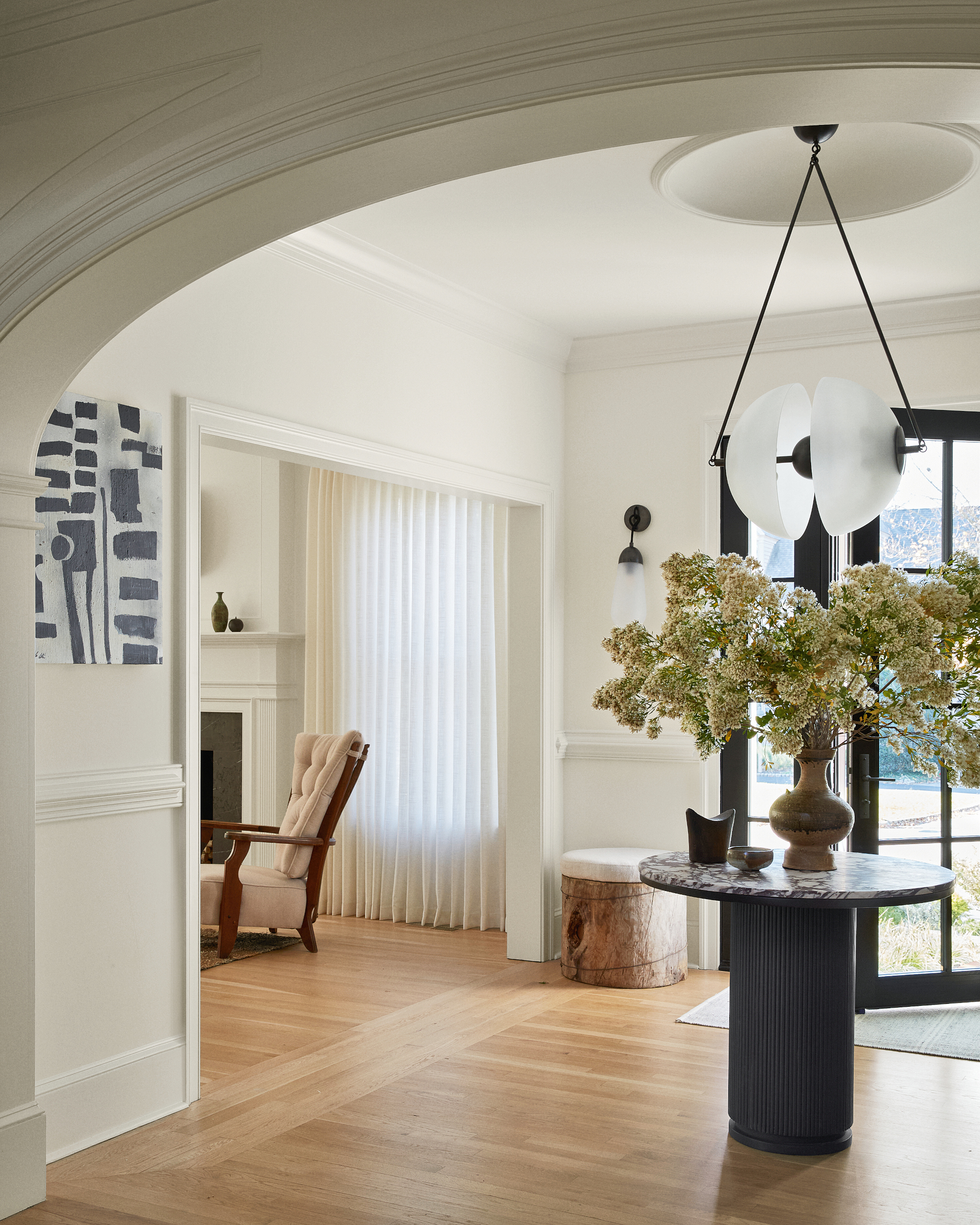 White entryway with architectural archway, black round pedestal table and brown vase with foliage