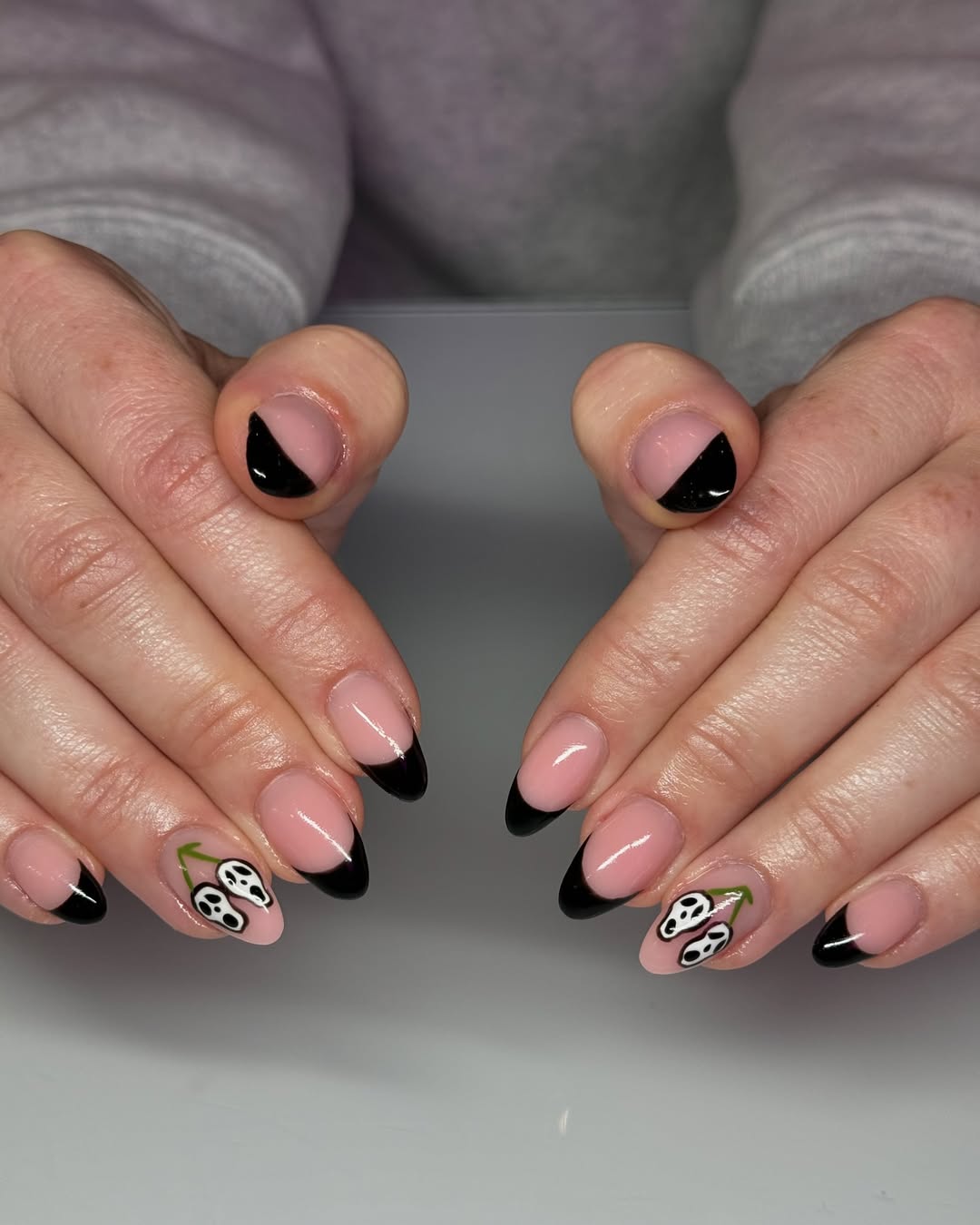a person wearing a black french manicure with a ghostface design on two fingers