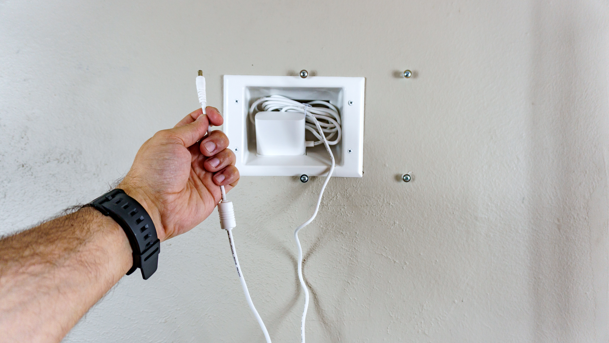A recessed outlet installed high up on a wall with a person holding a power cord in front of it