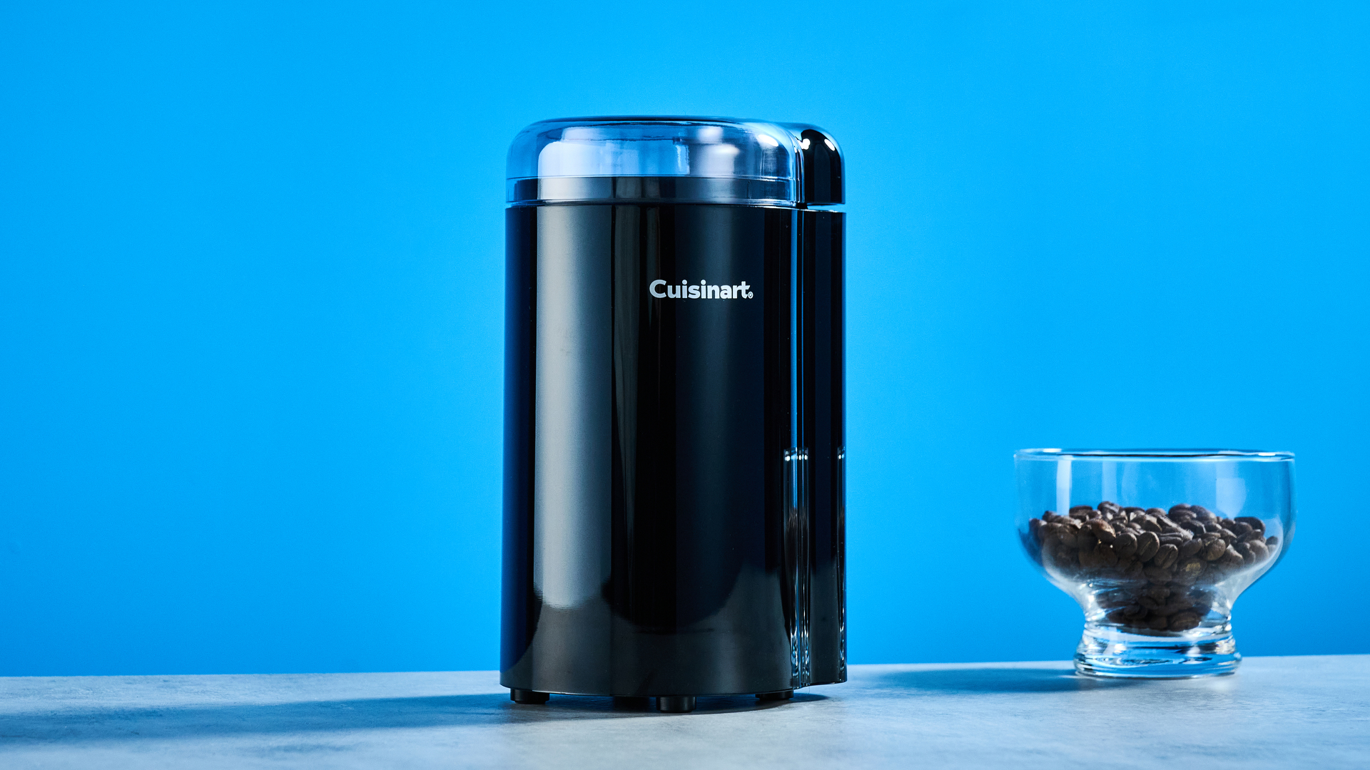 the cuisinart coffee grinder photographed against a blue background showing its blades and canister