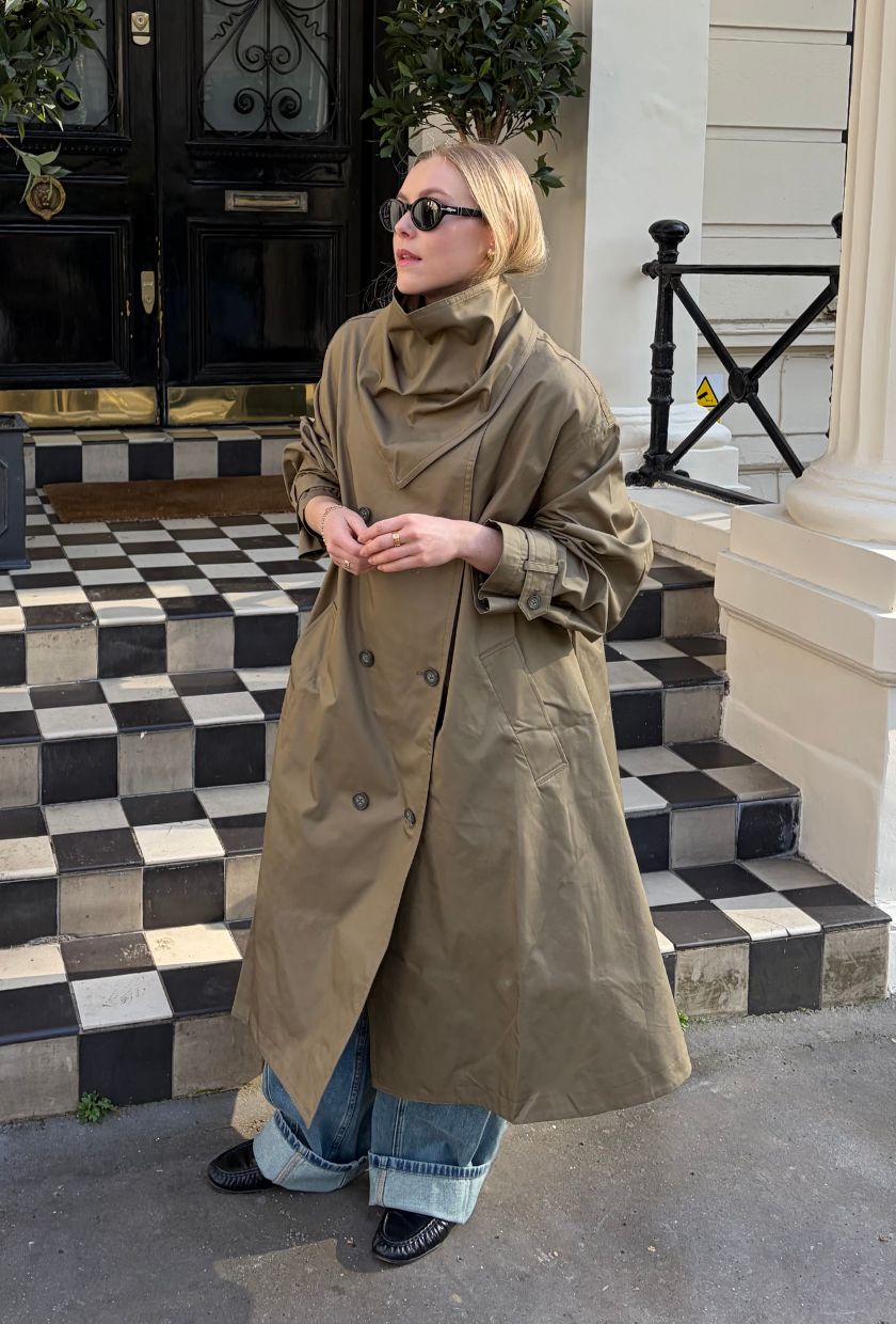 Woman wears beige trench coat, blue jeans and black loafers
