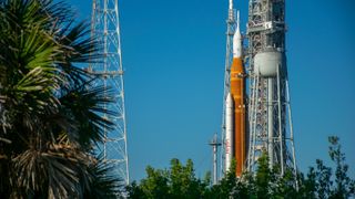 An orange rocket with a white top stands against a dynamic sky.