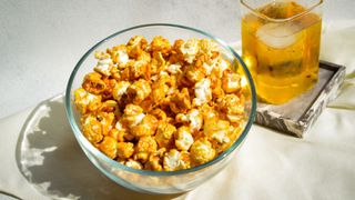 Bowl of flavoured popcorn sitting on tablecloth with juice in glass