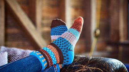 A pair of feet in fun socks are propped on the arm of a worn leather sofa.