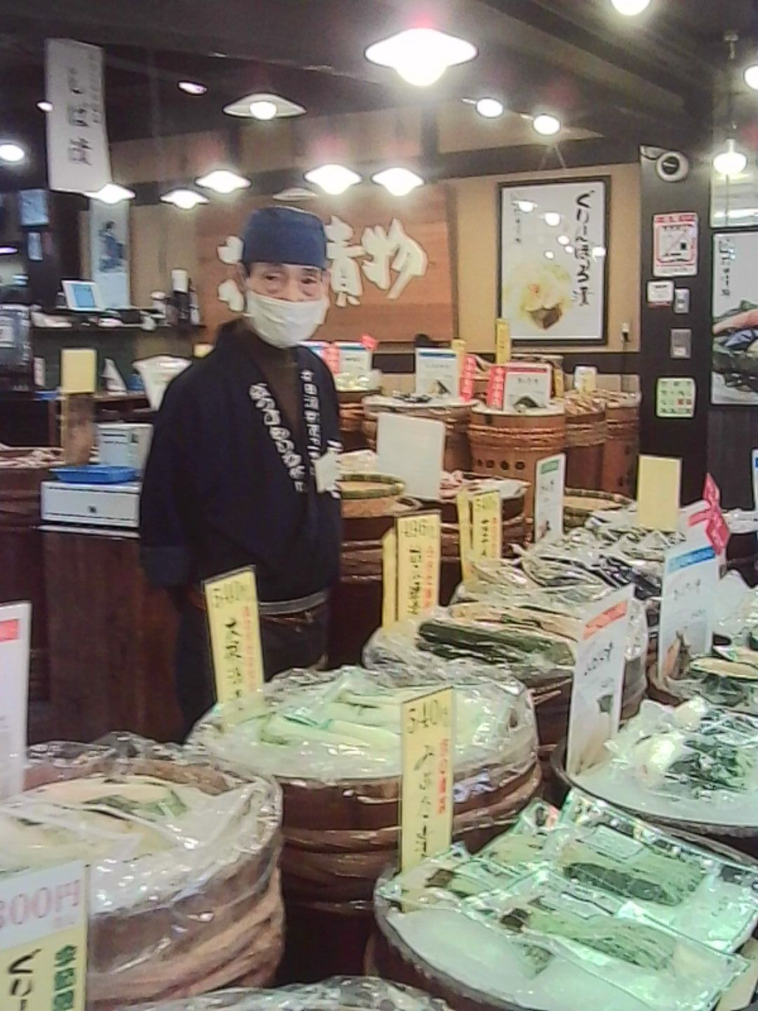 Japanese food shop counter filled with packaged goods and price signs.