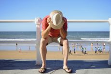 Man sitting with head in hands on boardwalk at beach.