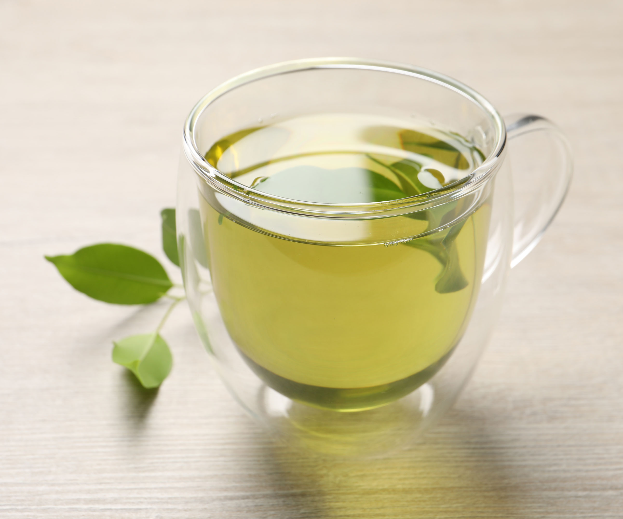 green tea in glass tea cup with leaves on worktop