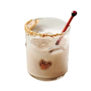 A glass with a squirrel motif on it, light brown liquid and ice cubes inside, and a dark red stirrer