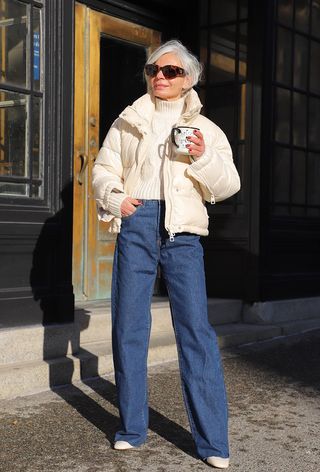 a roundup of the best puffer jackets shown in a photo of a woman wearing a white puffer coat over a white turtleneck sweater with wide-leg jeans and white ankle boots