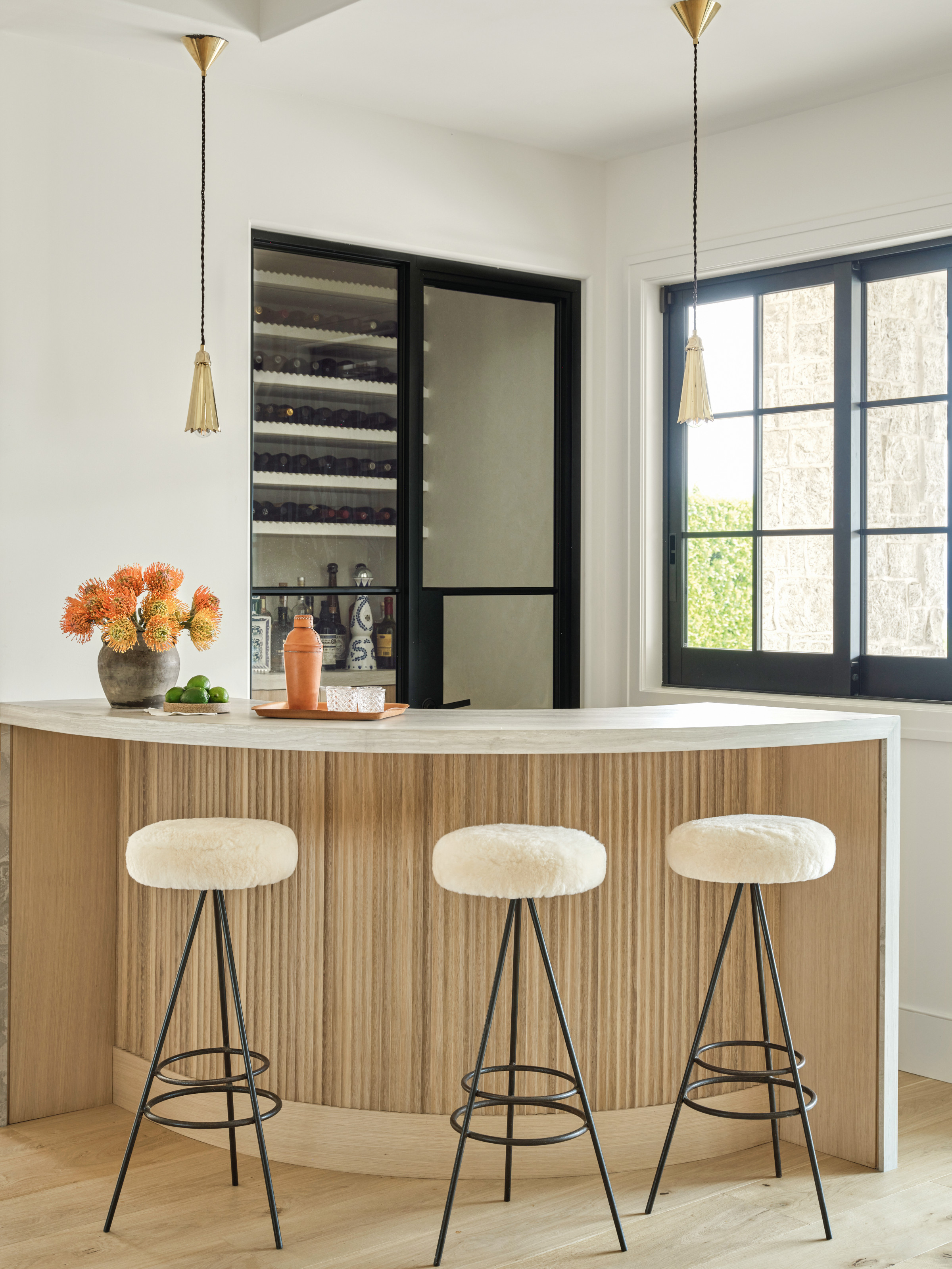 Home bar with fluted wood front, white countertop, white fleece-topped bar stools