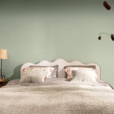A bedroom painted in Dulux's Soulful Sage shade with a bed with a wavy headboard