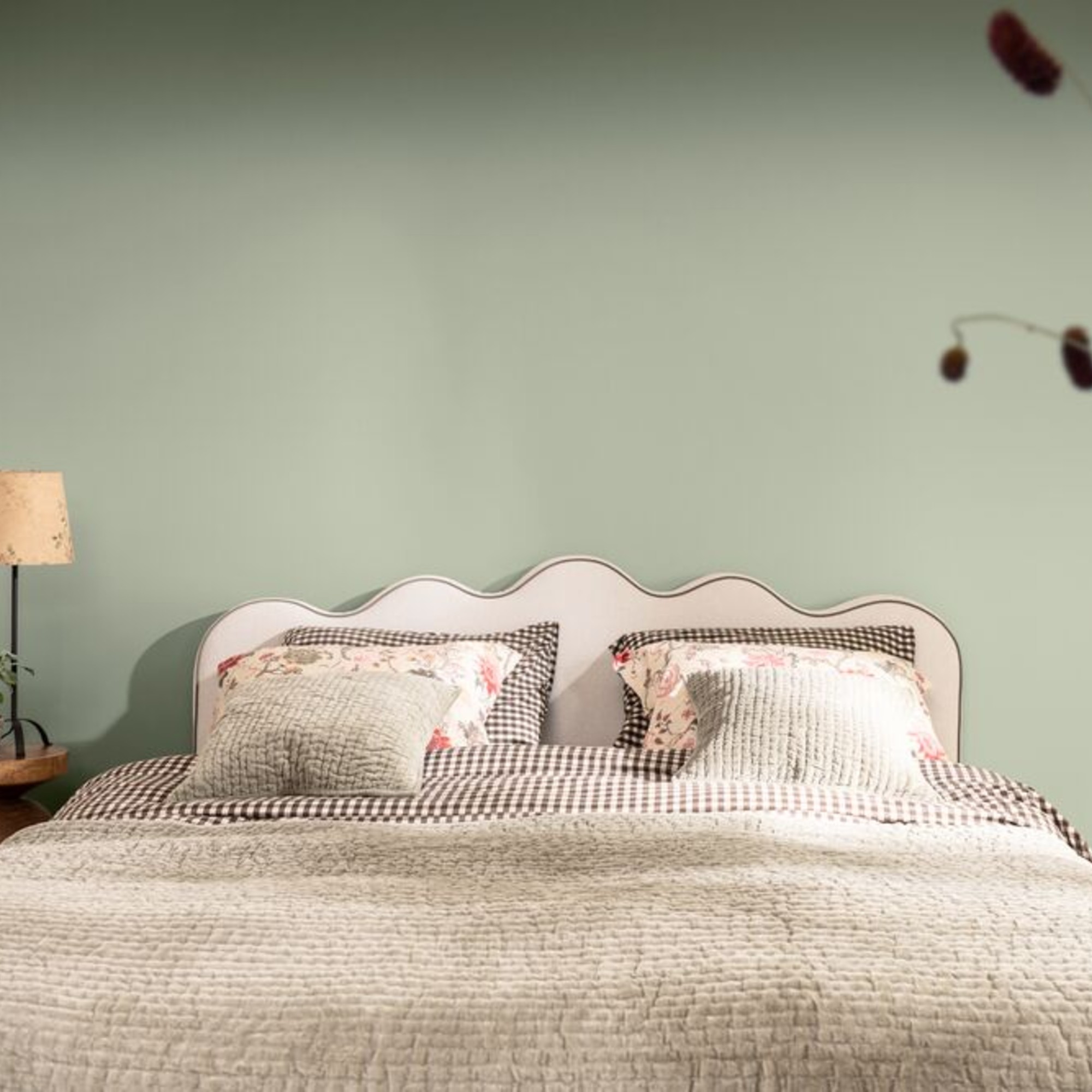 A bedroom painted in Dulux's Soulful Sage shade with a bed with a wavy headboard