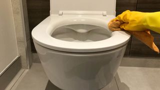 A toilet seat being cleaned with a microfiber cloth while wearing rubber gloves