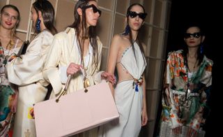 Models wear white coats, tops and trousers with light pink handbag