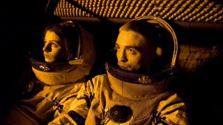 A still from the movie High Life. Here we have a close up of a man and woman wearing astronaut suits sitting next to each other.