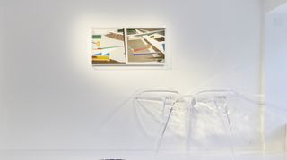 A see-through table is set against a wall. Above it is an abstract painting.