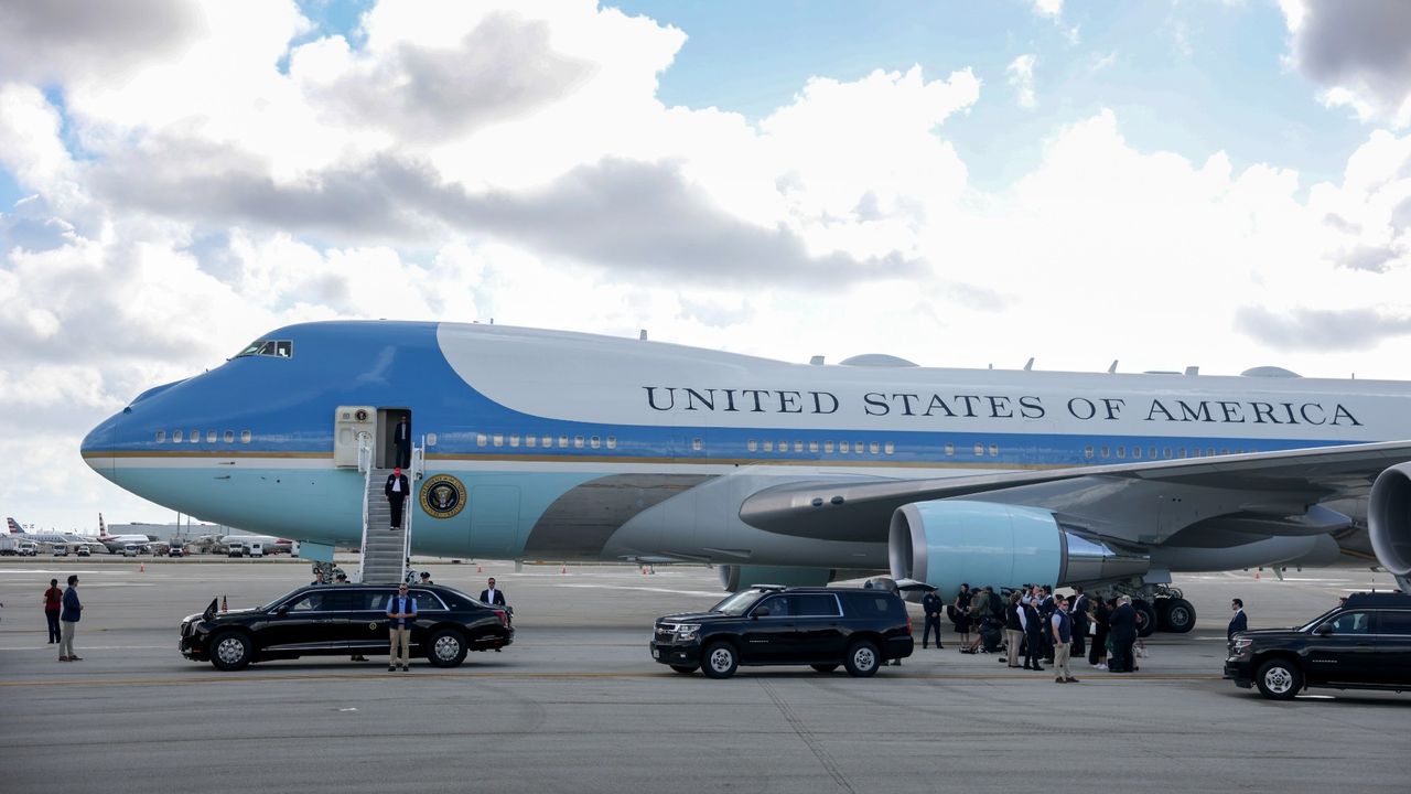 side shot of most of Air Force One having landed at an airport. a number of black cars are in front of the plane