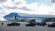 side shot of most of Air Force One having landed at an airport. a number of black cars are in front of the plane