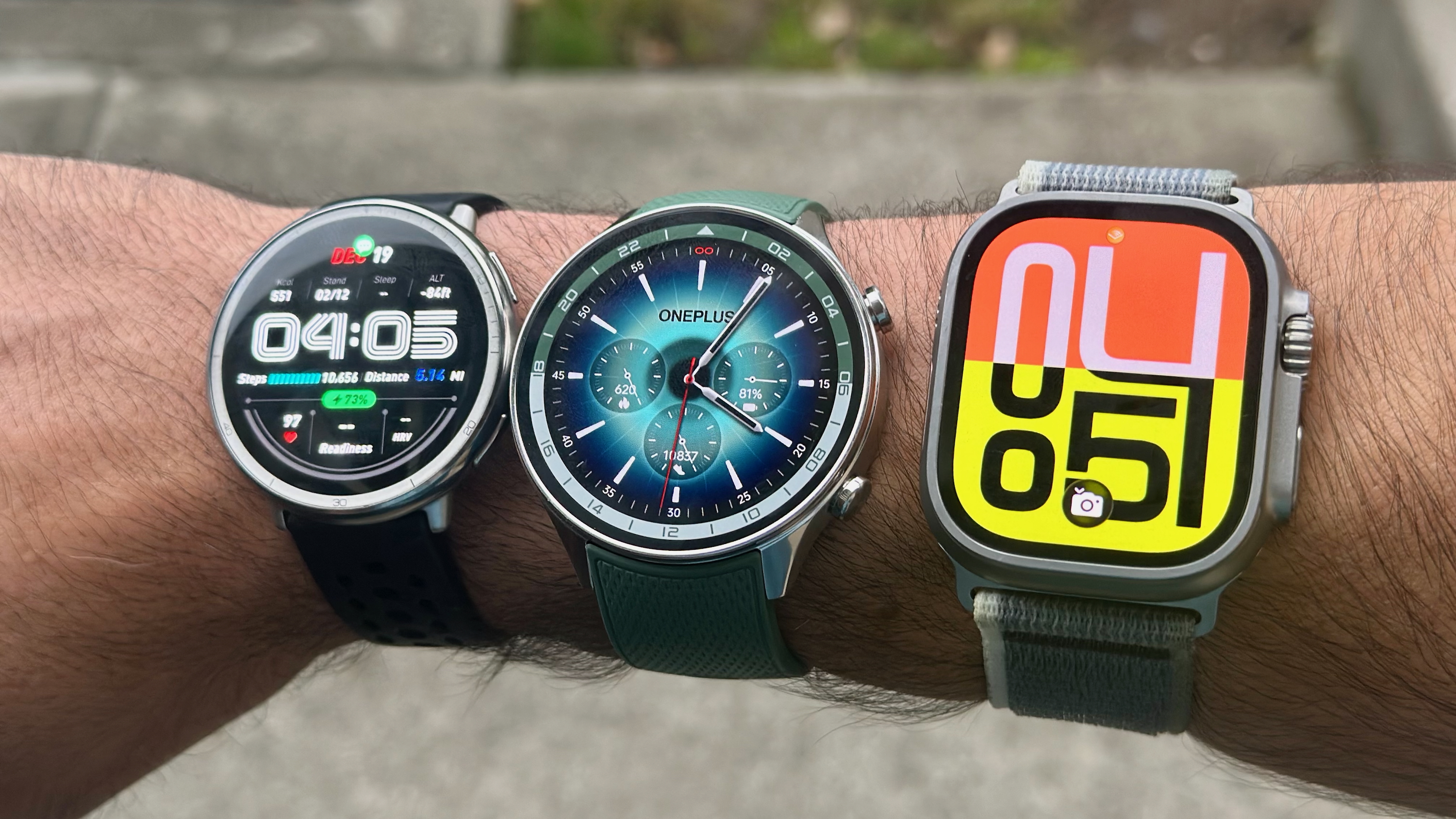 A photo of the Amazfit Active 2, OnePlus Watch 2R, and Apple Watch Ultra 2 all strapped onto one arm.