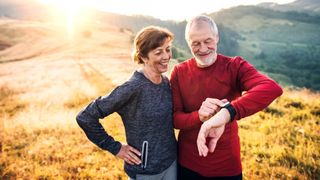 Couple pausing to look at smartwatch during hike at sunset