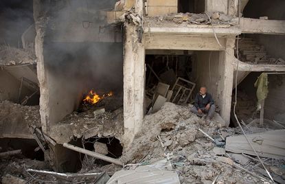 A man sits in the rubble of a building destroyed by an airstrike in Aleppo.