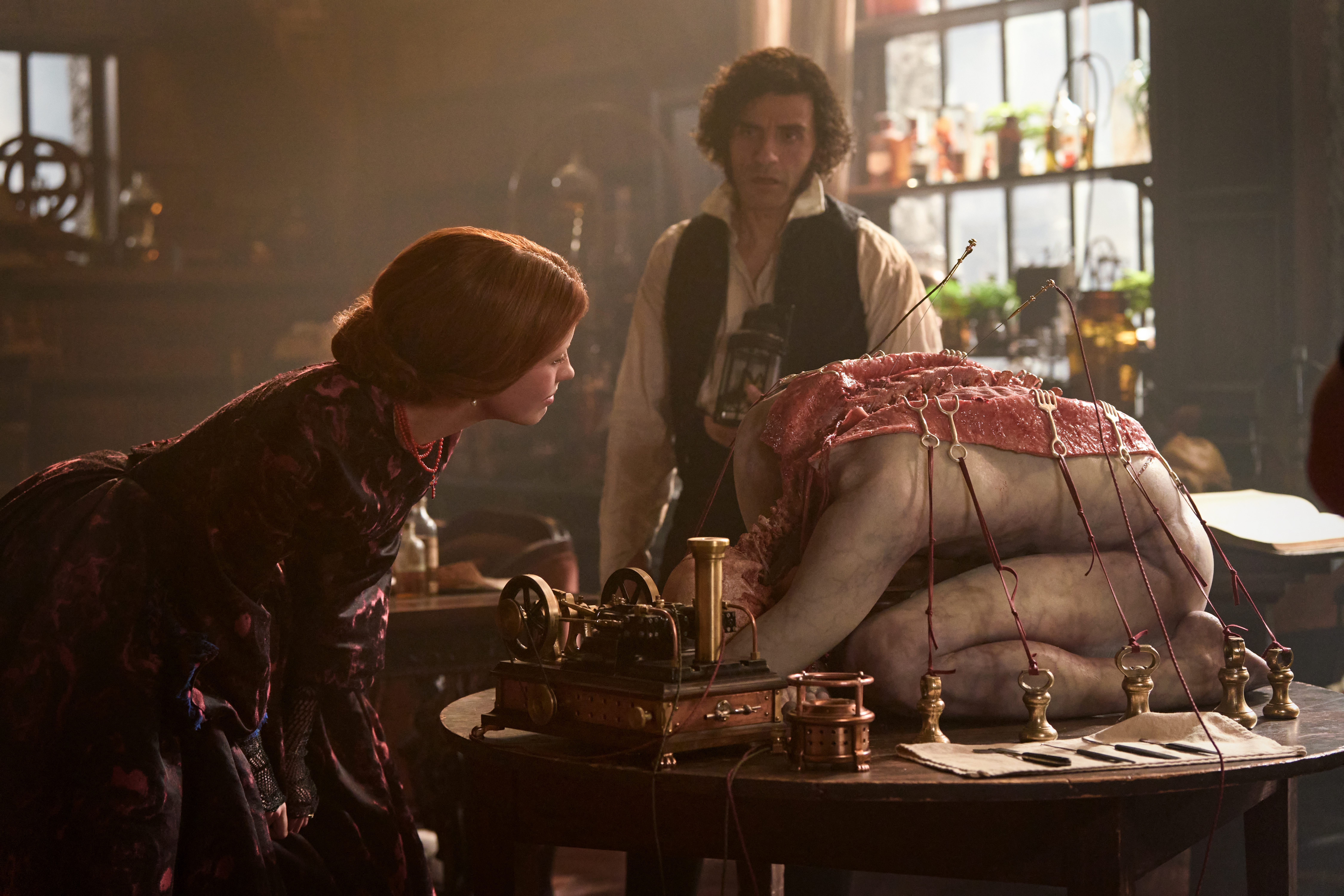 mia goth as elizabeth as she examines oscar isaac as victor&#039;s sewn open creation in his lab in a still from frankenstein