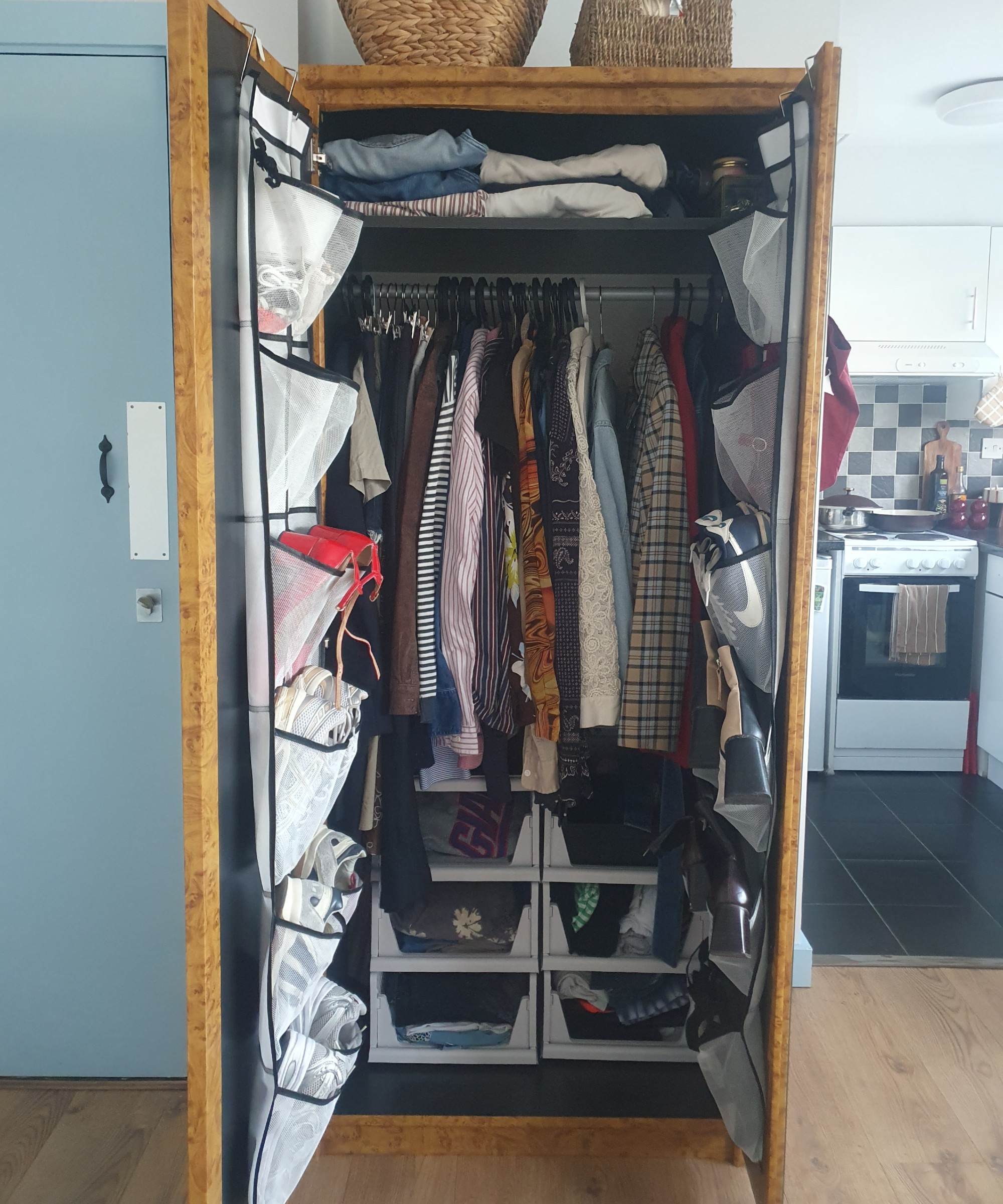 My wardrobe with open doors revealing its contents including the over-door shoe organisers and stackable storage baskets at the bottom