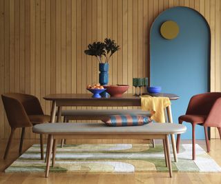dining room with wooden wall panelling, blue arched wall feature, wooden floor, large rug and walnut oval dining table with upholstered chairs and benches