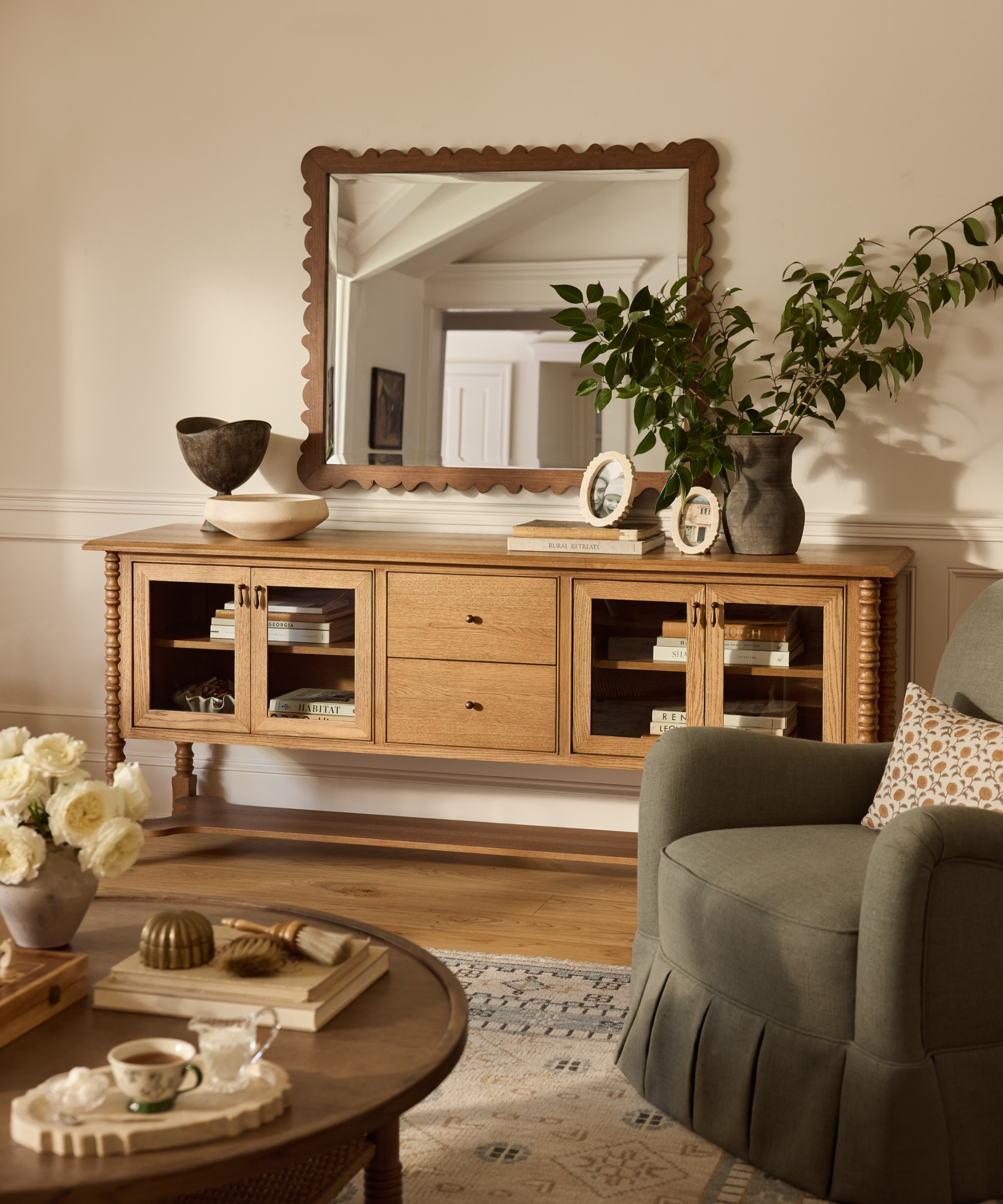 a living room with a large wood credenza, a decorative mirror, a green accent chair, and a coffee table in the foreground