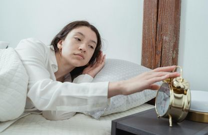 Young woman waking up in bed with alarm clock
