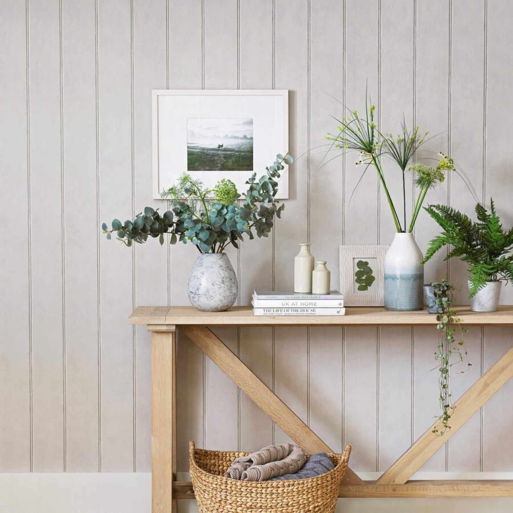 Room with traditional panelled wall painted light green, a wooden console table and wood flooring, with basket and plants and small group of accessories.