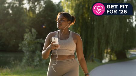 Black woman in athleisure walking in park with phone and earbuds