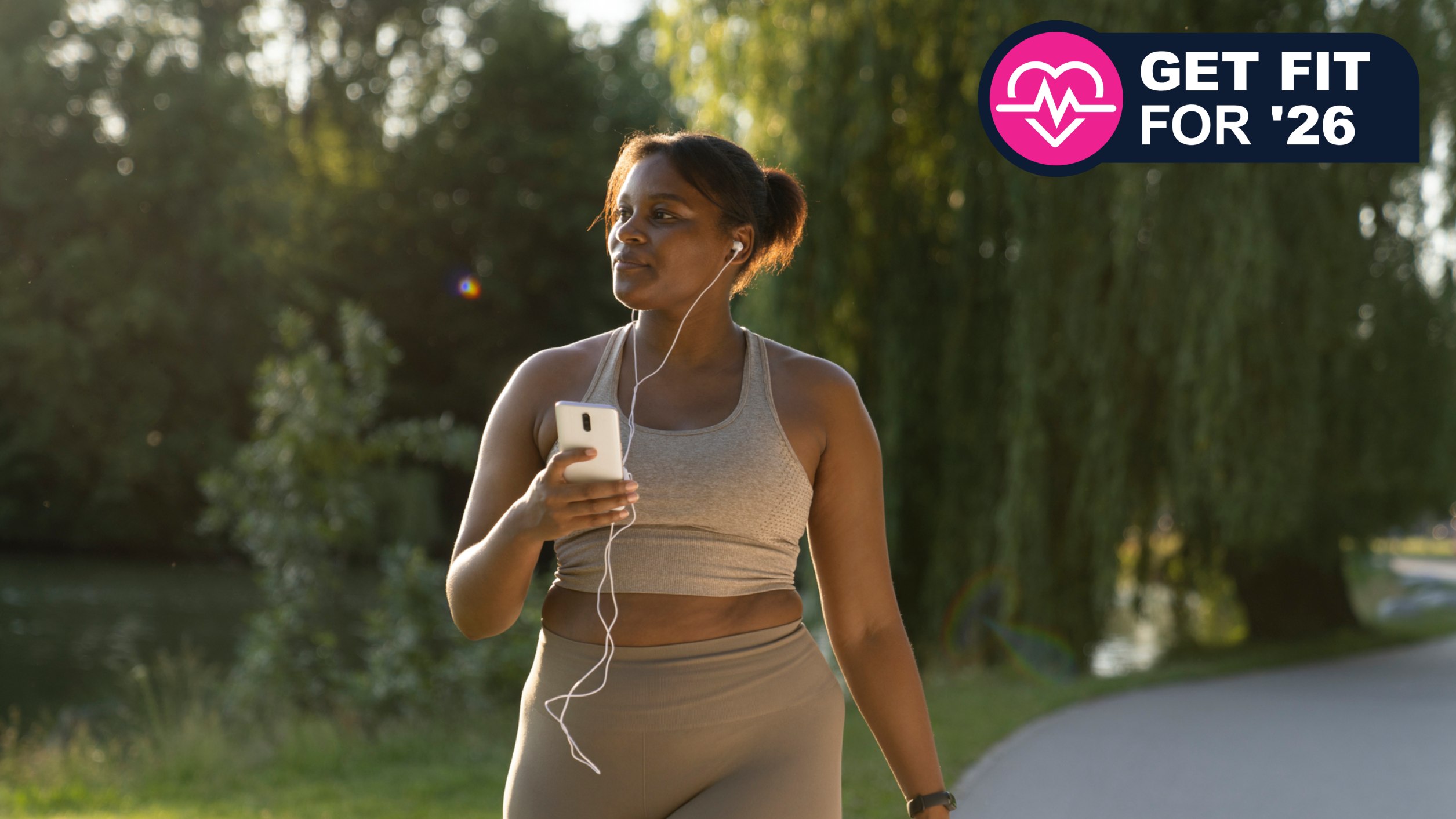Black woman in athleisure walking in park with phone and earbuds