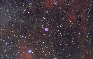 a star packed scene with diffuse regions of red gas and dust spread throughout and a distinct purple circle at the center of the image.