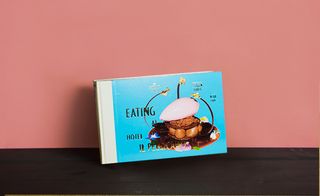 Front cover of the book 'Eating at Hotel Il Pellicano', blue background, black lettering, noodles, food dish image, dark wood surface, orange background