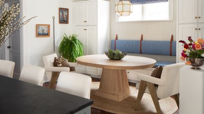 Breakfast nook with white walls and cabinets, round breakfast wood table, banquette seating and jute rug