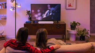Couple listening to Sonos Ray sat on sofa in front of TV