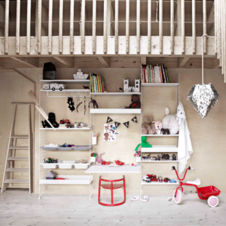 Neutral wall with open shelving unit containing books, toys and bunting, next to ladder and red tricycle